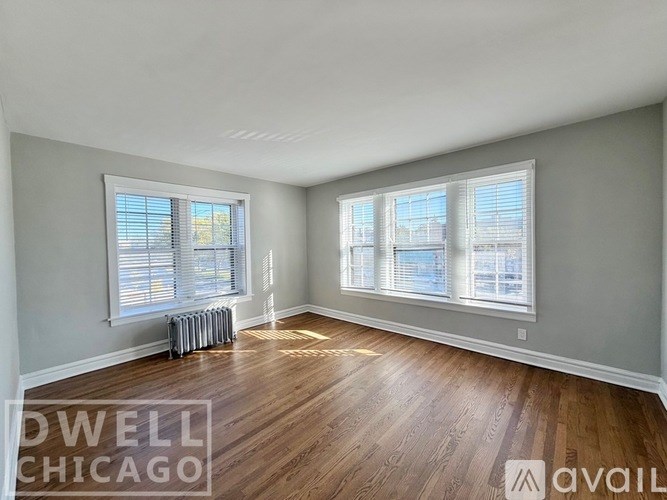 A room with wooden floors and two windows with blinds.