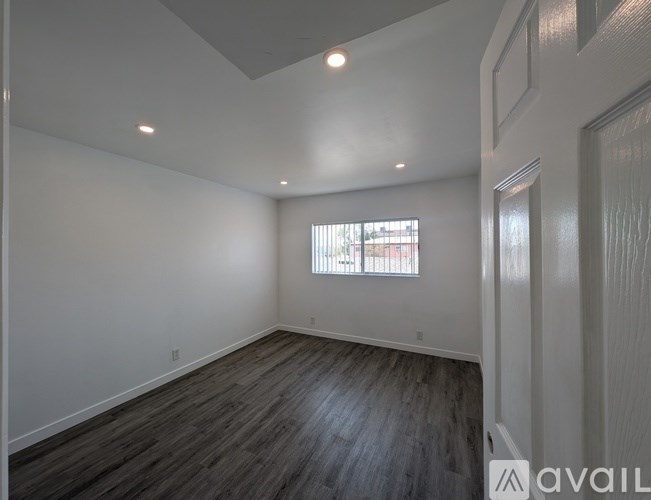 A spacious room with wooden flooring and a window with blinds.