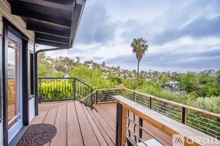 A balcony with a wooden floor and a metal railing overlooks a tree-filled landscape.