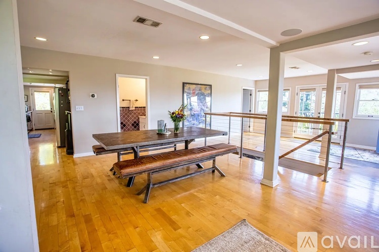 A wooden table with benches is in the middle of a room with a glass door leading to a balcony.