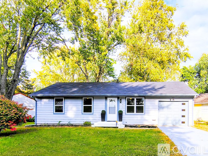 A small house with a white garage door is surrounded by greenery.