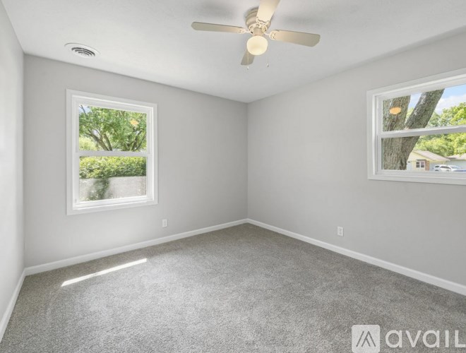 A room with a ceiling fan and two windows.