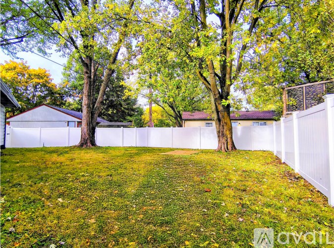 A white fence encloses a grassy yard with trees.