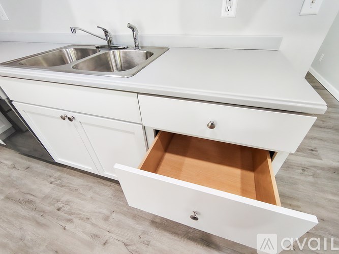 A white kitchen with a sink and a drawer pulled out.