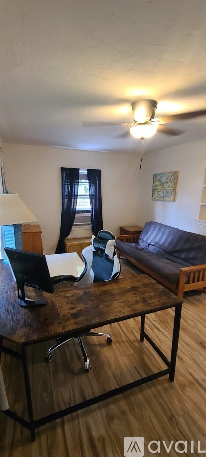 A room with a ceiling fan and a table with a computer on it.