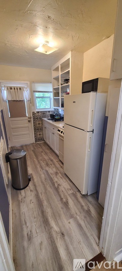 A kitchen with a white refrigerator and a trash can.