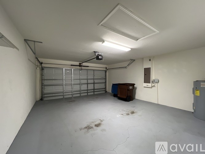 A large, empty garage with a white ceiling and a brown trash bin.