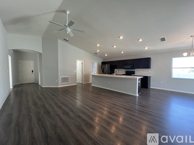 A spacious living room with a dark wood floor and a ceiling fan.