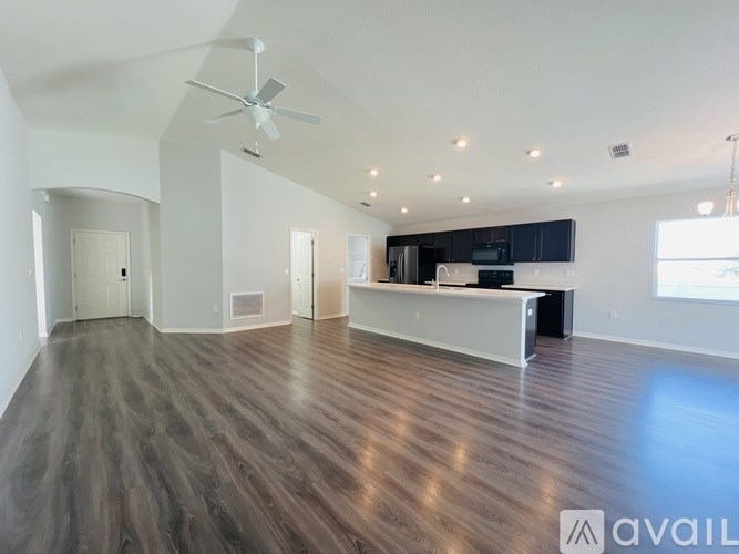 A spacious living room with a dark wood floor and a ceiling fan.