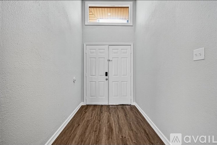 A white door is in a room with a wooden floor and a window with blinds.