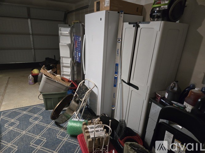 A white refrigerator is in a cluttered room with a blue rug on the floor.