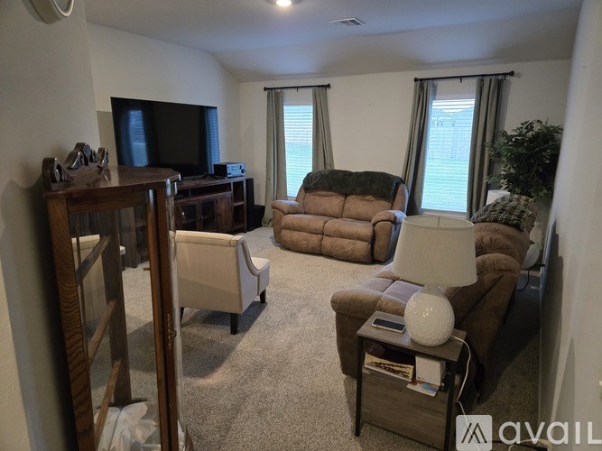 A living room with a brown couch, a brown chair, a brown ottoman, a white lamp, and a TV on a wooden stand.