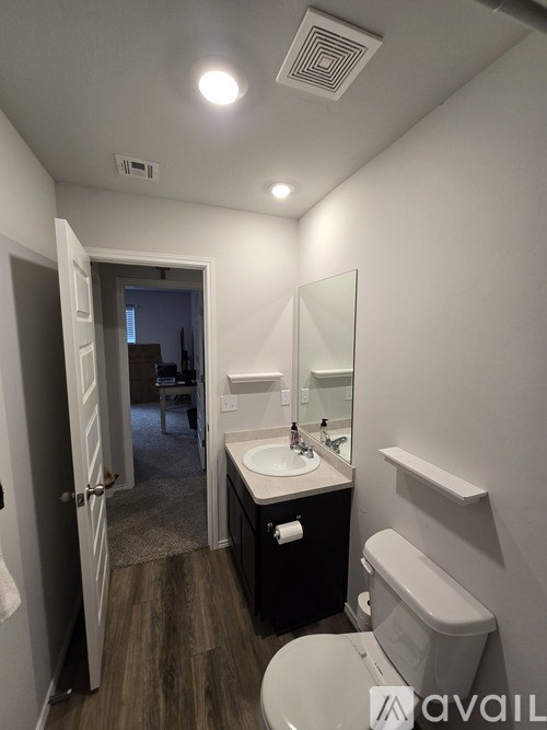 A bathroom with a toilet, sink, mirror, and a door leading to another room.