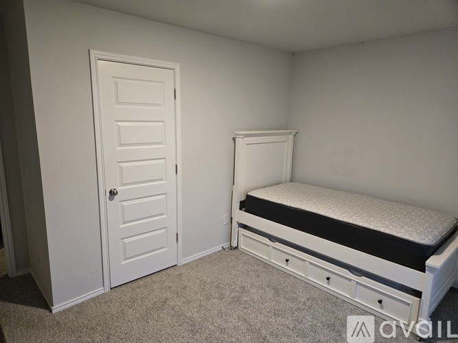 A white bed with a black mattress is in a room with white walls and a white door.