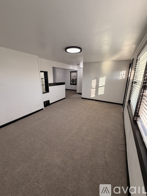 A spacious room with a carpeted floor and a window on the right side.