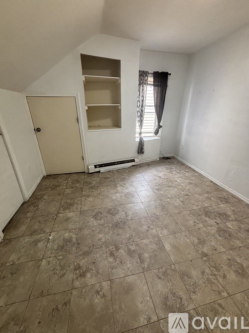 A room with a brown floor and a white wall with a cabinet and a window.