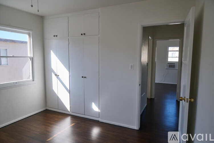 A room with white walls and wooden floors, with a window on the left and a door on the right.