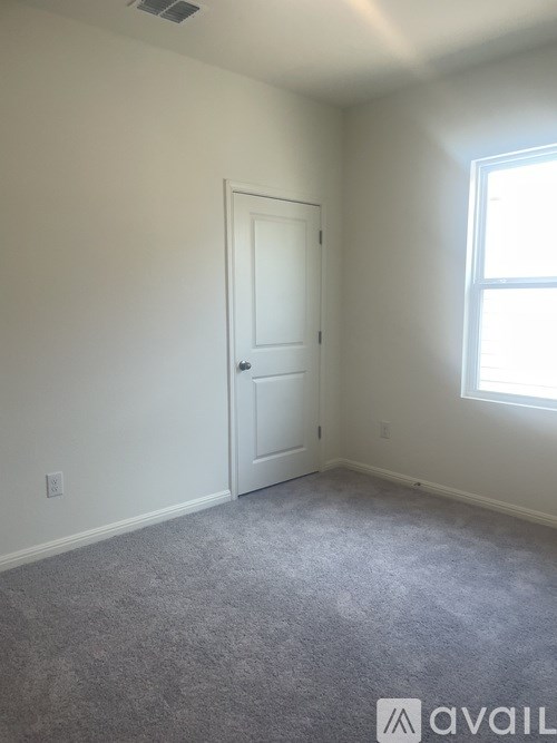 A room with a carpeted floor, a white door, and a window letting in natural light.