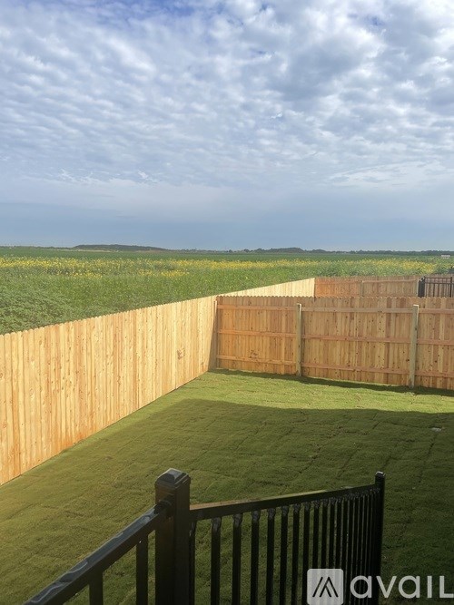 A wooden fence encloses a green lawn with a view of the countryside.