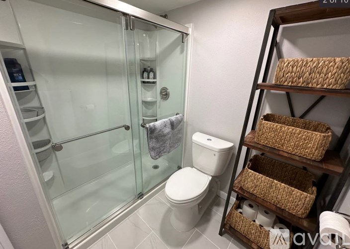 A small bathroom with a toilet, a glass shower stall, and a shelf with baskets on it.