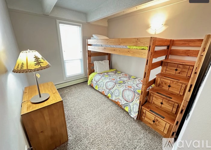A bedroom with a bunk bed and a wooden nightstand with a lamp on it.