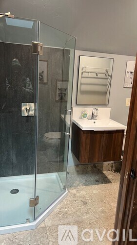 A bathroom with a glass shower stall and a sink with a mirror above it.