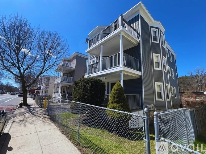 A grey apartment building with a tree in front.