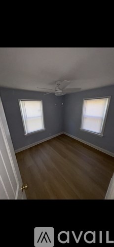 A room with wooden flooring and two windows.