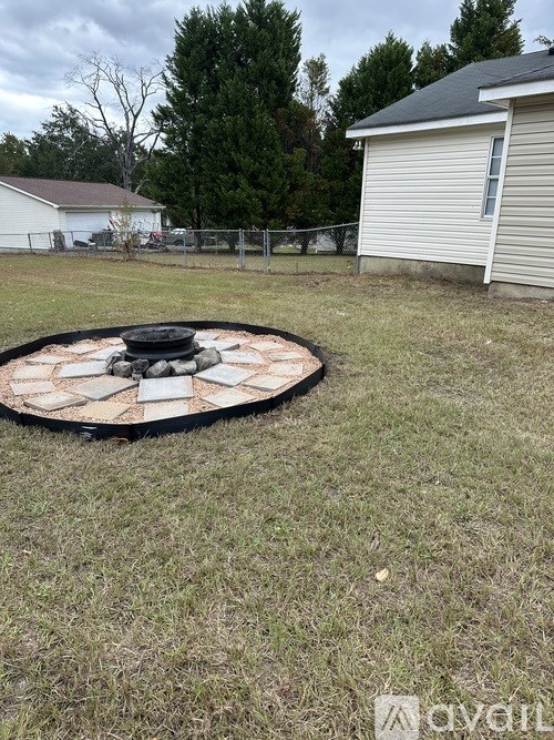 A fire pit in a backyard with a white house and trees in the background.