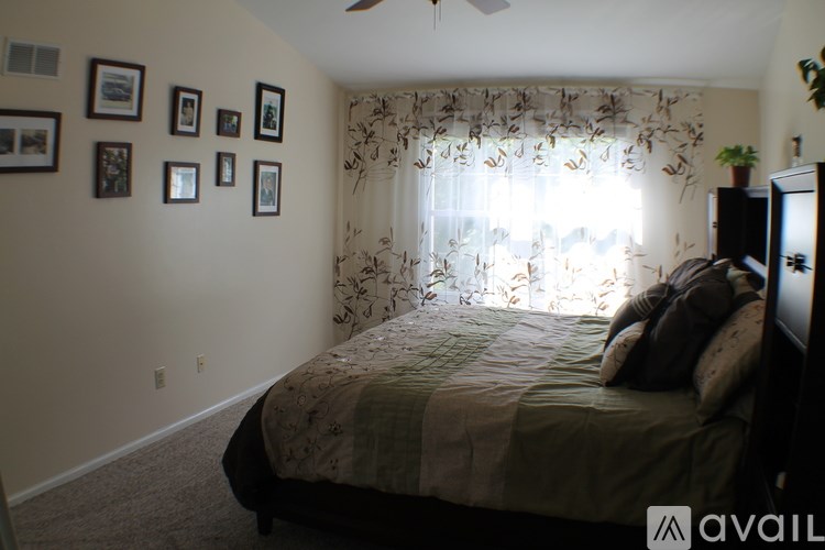 A bedroom with a bed, a window with curtains, and pictures on the wall.