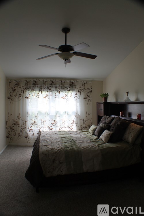 A bedroom with a bed, pillows, a ceiling fan, and a window with curtains.