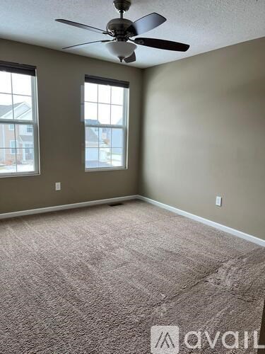 A room with a ceiling fan and two windows.