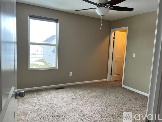 A room with a ceiling fan and a door leading to another room.
