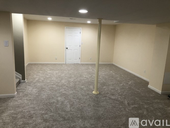 A spacious room with a carpeted floor, a white door, and a light on the ceiling.