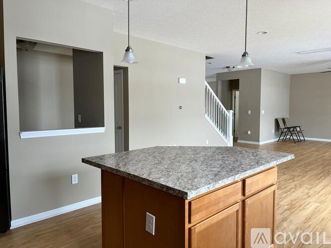 A kitchen island with wooden cabinets and a granite countertop in a room with a staircase in the background.
