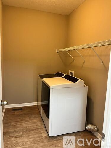 A white washing machine in a small room with a shelf above it.