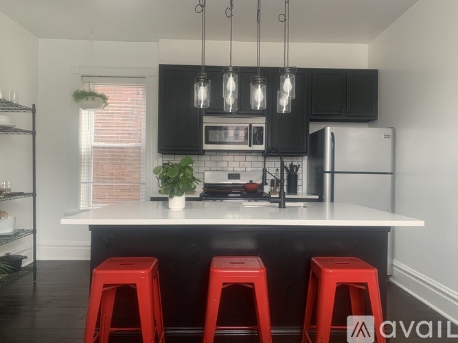 A kitchen with black cabinets and a white countertop with red stools.