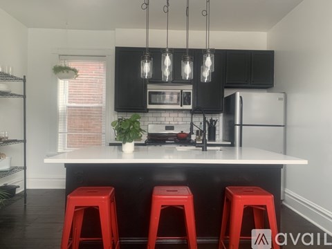 A kitchen with black cabinets and a white countertop with red stools.