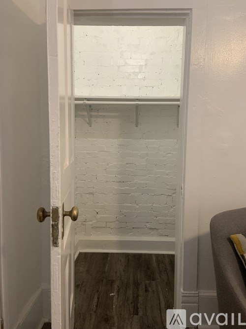 A white door with a gold handle is open to a room with a white brick wall.