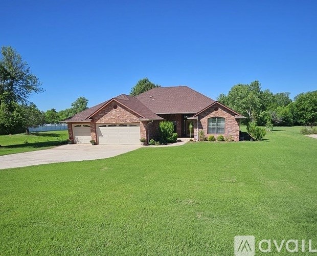 A house with a brown roof and a garage is surrounded by a green lawn.