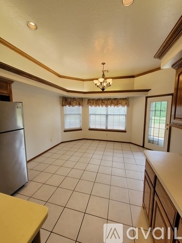 A kitchen with a refrigerator, a chandelier, and a window with curtains.