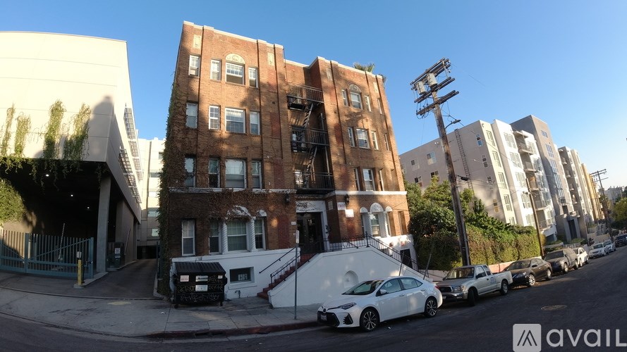 A white car is parked in front of a brown building.