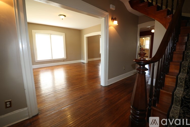 A hallway with a wooden floor and a staircase on the right side.