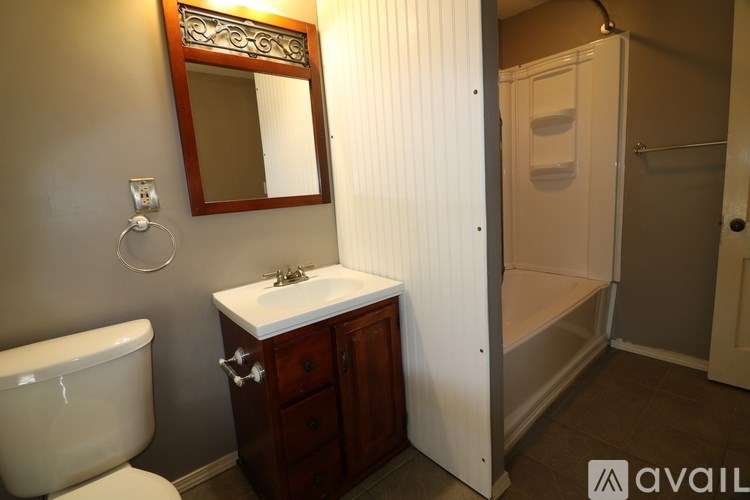 A bathroom with a white toilet, a sink with a wooden cabinet and a mirror above it.