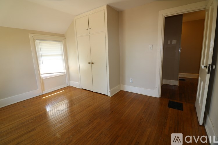A room with wooden floors and white walls, with a window on the left and a door on the right.