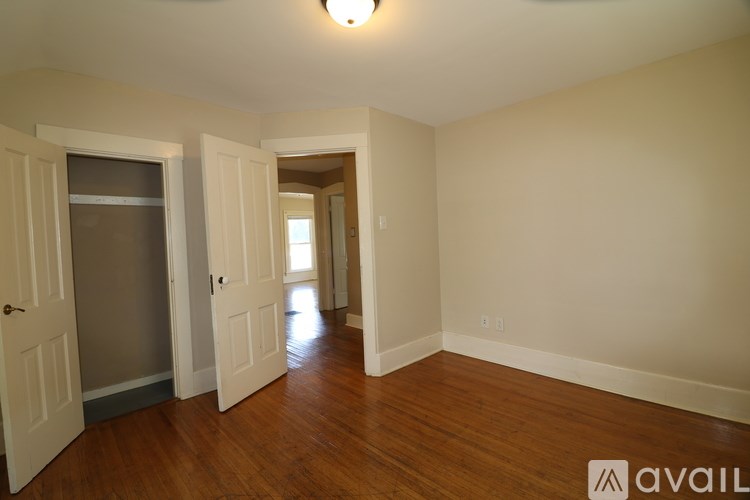 A room with wooden floors and white walls, with a door on the left and a window on the right.