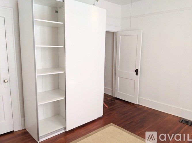 A white wardrobe with a mirror above it is in a room with a beige rug on the floor.