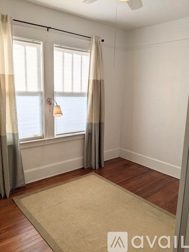 A room with a rug, a window with curtains and a fan.