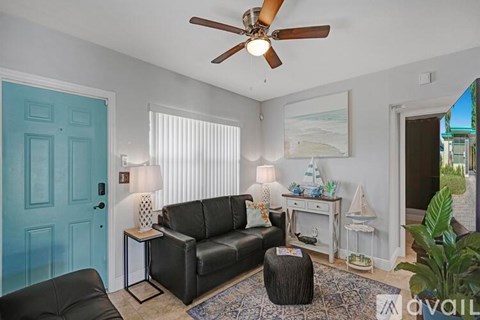 A living room with a black leather couch and a ceiling fan.