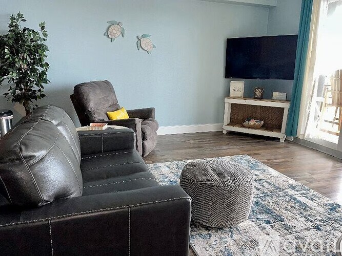 A living room with a black leather couch and a grey ottoman.